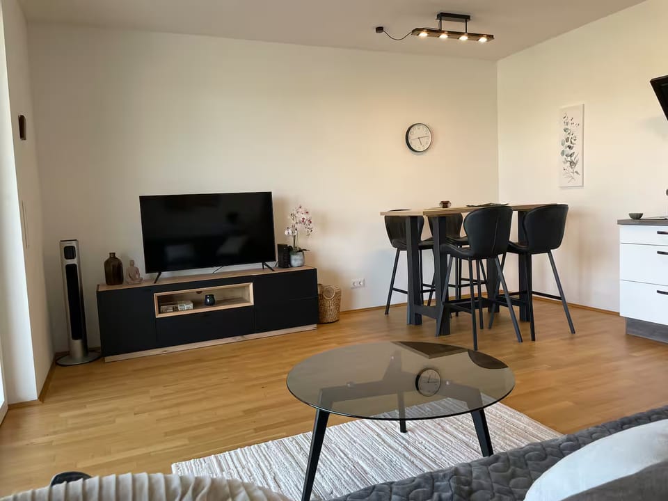Essbereich mit Stehtisch und vier schwarzen Barhockern, links TV-Möbel mit Fernseher