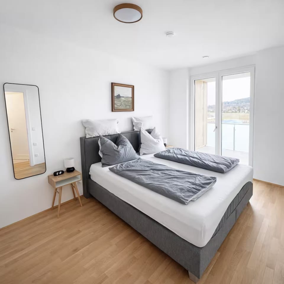 Schlafzimmer mit Doppelbett, Nachttisch und Wandspiegel, Glastür zum Balkon